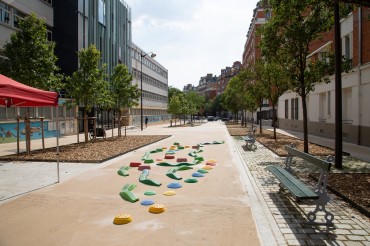 une rue piétonne avec des arbres, des bancs, des jeux pour enfants au sol